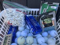 Overall lot showing basket filled with golf balls, tees, Dunlop boxes, packaged putting aids and digital device