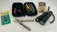 Full lot showing packaged accessory, multitool pliers, zip case of tools, packaged flashlight and two loose flashlights