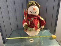 Front view of stuffed fabric snowman with skis, tape measure shows width