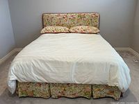 Full view of queen bed with floral headboard, skirt, shams, white bedding