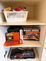 Cabinet shelf showing boxed drill, bit set, pliers in tool roll, extras