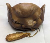 Front view of carved wood devil head bell showing facial features and tongue clapper