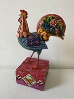 Front left view of multicolor rooster on red square pedestal