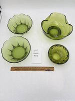 Four green glass bowls of differing sizes and designs displayed with ruler