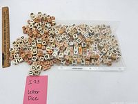 Bulk pile of mixed letter dice beside ruler and note indicating lot