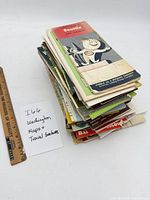 Stack of approximately 60 folded Washington travel maps and brochures beside ruler for scale