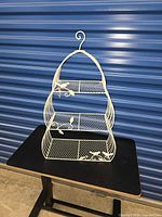 Front view of cream metal three-tier birdcage shelf on table