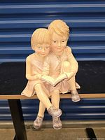 Front view of figurine showing two children reading book, legs hanging