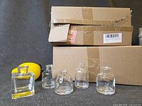 Two sealed boxes with five sample clear glass bud vases displayed in front