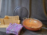 Group shot showing wok with lid, bread slicing board, pizza pan, and two dish towels