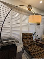 Full view of chrome arch floor lamp beside chair and stereo
