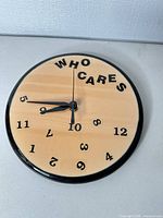 Front view of round wood-face wall clock showing WHO CARES design and scattered numbers