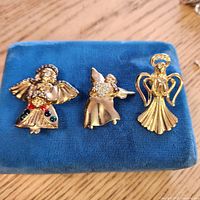 Front view of three gold-tone angel brooches on blue pad