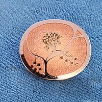 Front view of oval brooch on fabric, showing enamel floral design and copper tone texture