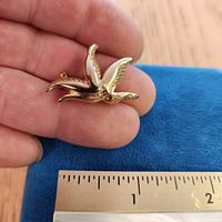 Front view of gold-tone bird brooch beside ruler showing size