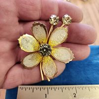 Brooch front view held in hand showing petals, center rhinestone and ruler measurement