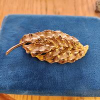 Front view of gold-tone leaf brooch on blue background