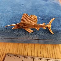 Gold-tone sailfish brooch resting on blue cloth