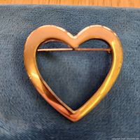 front view of open heart gold tone brooch on cloth