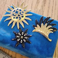 Overview showing all three brooches: sun, abstract fan, floral starburst