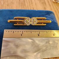 Front view showing gold-tone bar brooch with heart rhinestone center next to ruler for scale