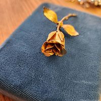 Front view of gold-tone rose bud brooch on blue fabric