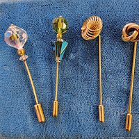 All four gold-tone stick pins displayed on fabric