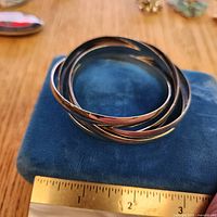 stack of five silver-tone bangles on blue box with ruler showing diameter