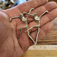 front view of silver-tone dancers brooch held in hand next to ruler