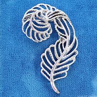 Front view of silver-tone feather brooch on blue cloth