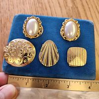 Front view of five clip-on brooches on blue pad with ruler for scale
