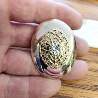 Front view of oval gold tone brooch showing filigree pattern and rhinestone