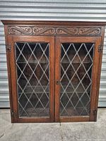 Front view of oak cabinet showing twin leaded glass doors and carved crest