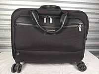 Front view of black Briggs & Riley rolling brief showing leather handles, front zip pocket and four wheels