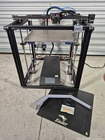 Overall view of Creality Ender cube-frame 3D printer with build plate and accessories on floor
