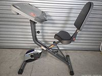 Side view of folded ExerWork exercise bike showing frame, seat, backrest and flywheel