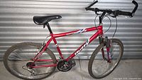 Full left-side view of red Huffy 26-in mountain bike against metal wall