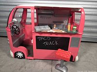 Overall view of pink food truck with stool, chalkboard, driver’s cab and interior kitchen visible