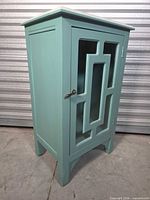 Front left view of teal cabinet showing door handle and glass inserts