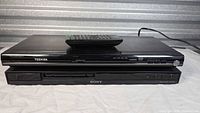 Stacked Toshiba and Sony DVD players with remote on top