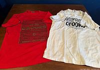 Red and white Crooks & Castles graphic T-shirts laid flat side by side on table
