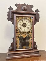 Front view of Victorian Eastlake wood mantel clock showing carved case and glass door with gold stencil