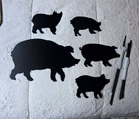 five black metal pig silhouettes and bundled stakes displayed on white surface