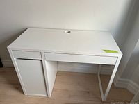 Front view of white desk showing closed drawers, cabinet door and cable grommet