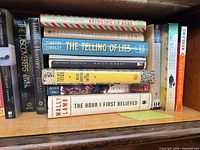 Stacked and shelved books including Bringing Up Bébé, The Telling of Lies, Anil’s Ghost, Border Songs, The Hour I First Believed plus vertical row with Tim O’Brien, The Discoverers etc.