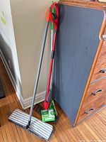 Three handled mops and box of Swiffer cloths leaning against dresser
