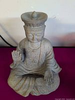 Front view of gray cast concrete seated statue showing raised hand and robe detail