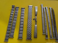 Eight stainless steel watch bands arranged on yellow background