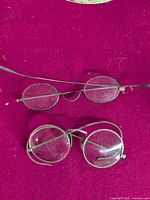Two pairs of round wire eyeglasses on magenta cloth