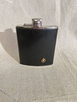 Front view showing black leather exterior, silver rim, gold emblem and screw cap